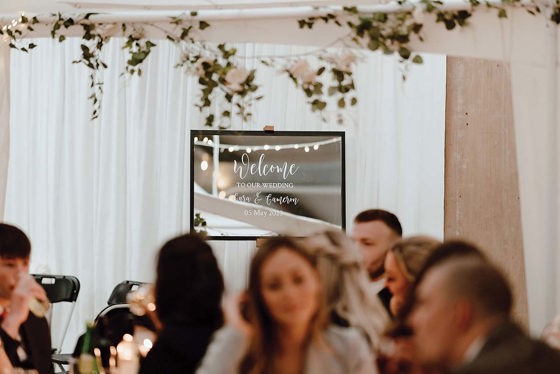 Welcome to our wedding sign painted on a mirror in reception hall with tables of people surrounding it